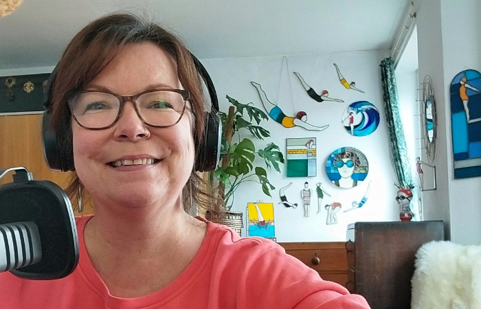 Charlotte Savill in foreground wearing headphones with her stained glass swimmers on the wall in the background.