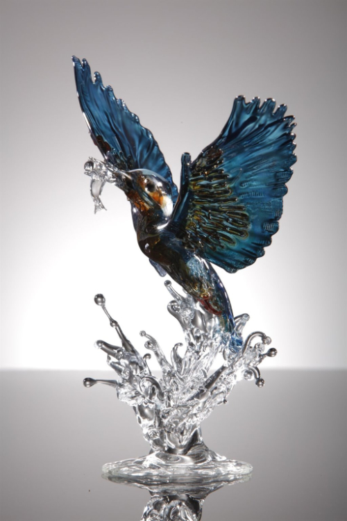 Lampworked glass sculpture of a kingfisher taking off from a splash of water.