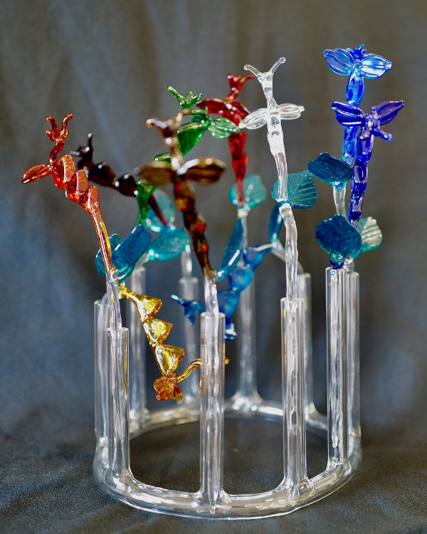 Sculpture made using lamp working featuring clear glass circular base with clear glass verticals supporting colourful glass creatures that look a bit like Nessie the Loch Ness monster.
