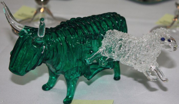 Lampworked green glass highland cow being kicked in the side by a calf in clear glass.