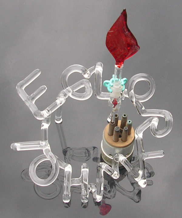 Humorous lampworked glass sculpture called 'Glory Whole' featuring end of lamp working torch and red glass flame and words made from clear glass.