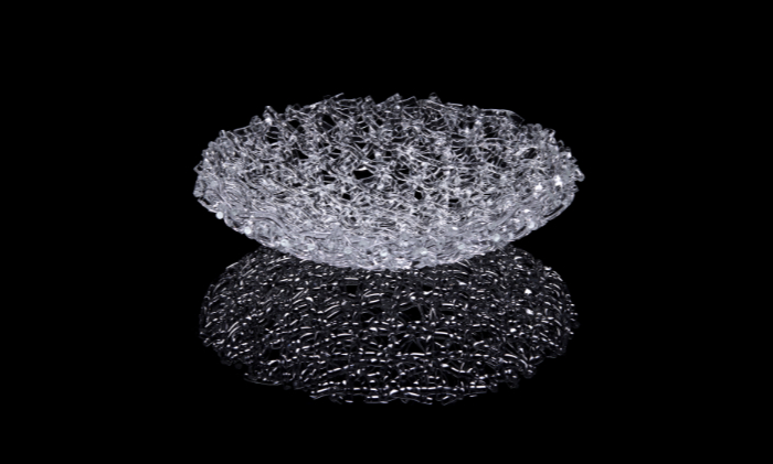 A clear glass sculpture intertwining many part-melted rods of glass in a woven effect, called Hoarfrost, photographed against a black background and reflected beneath.