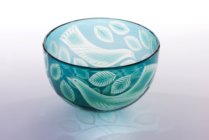 An aqua blue bowl decorated with birds and leaves created through sandblasting the surface of the glass.