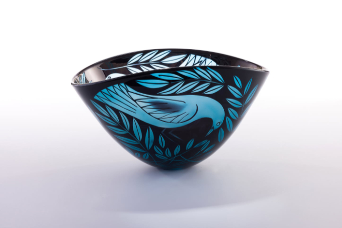 A black and blue blown glass bowl featuring a bird and leaf design sandblasted on the surface.