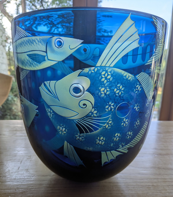 A large glass vessel in blue glass featuring different shaped and decorated fish sandblasted onto the surface.