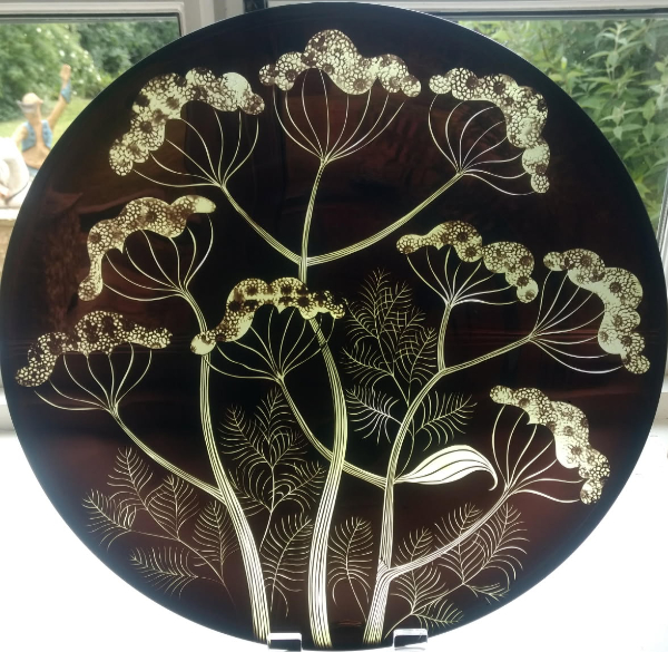 A large, round glass plaque made from brown glass and sandblasted with a design of curving flowers and leaves. 