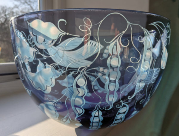 A large, wide glass bowl in pale grey-brown featuring pea pods and birds in white that have been sandblasted onto the surface.