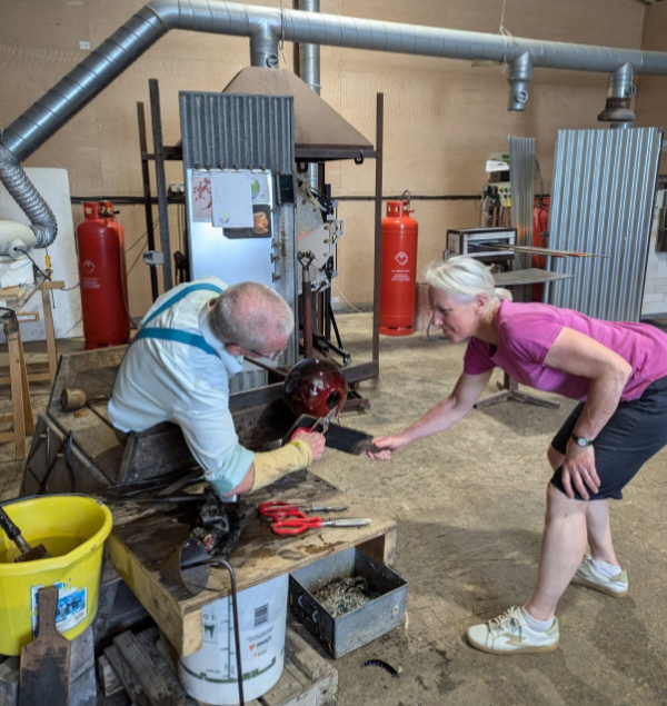 A view of a glassblowing studio with Ruth Dresman assisting Neil Wilkin to shape molten glass to her design.