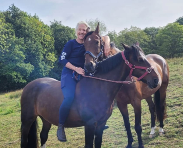 Glass artist Ruth Dresman sitting bareback on one of her horses and holding the neck of the other in a hug.