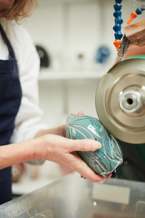 Close up image of Michele Oberdieck cutting marks into a small, coloured glass vessel on the lathe.