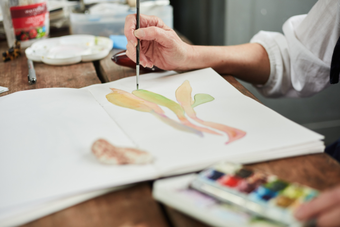 Close up shot of Michelle Oberdiek's hands as she paints a glass idea in a sketchbook in pastel shades.