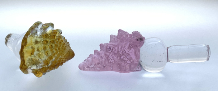 Glass bottle stoppers featuring Romanesco-inspired sculptures in pink and amber-green attached to clear glass stoppers.