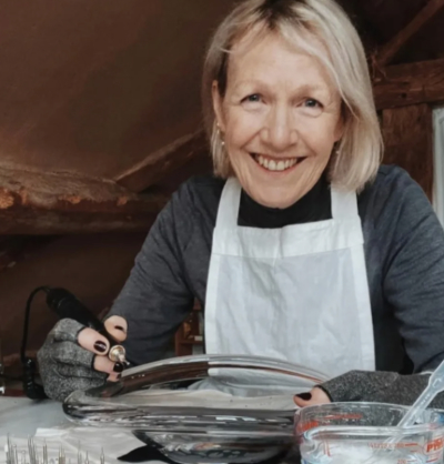 Glass engraver Nancy Sutcliffe smiling at camera as she works on engraving a clear glass shallow bowl.