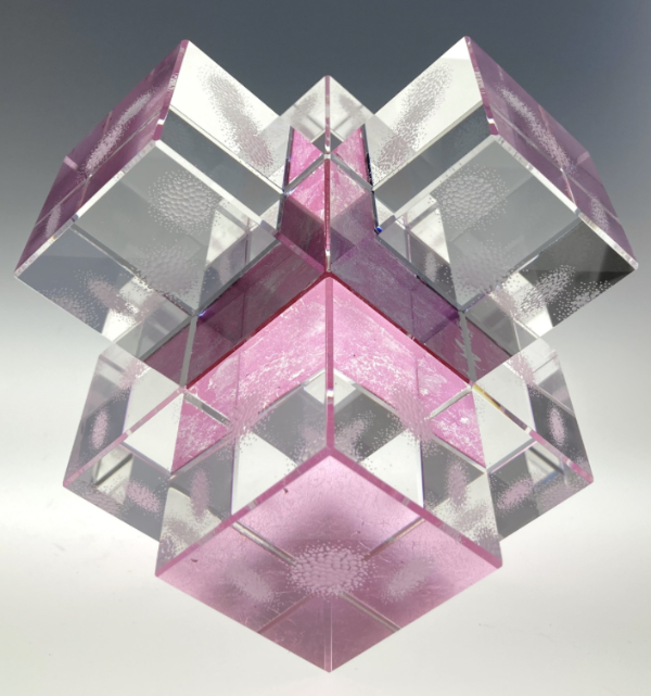 A glass engraved piece called Geode featuring square and rectangular glass pieces of polished glass set together in a 3D unit, with pink highlights and fine engraving reflected throughout. Made by Nancy Sutcliffe.