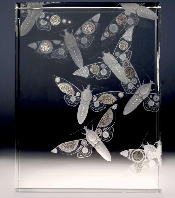 Stylised moths engraved on a block of polished glass featuring patterned wings and bodies with gold leaf highlights. Made by Nancy Sutcliffe.