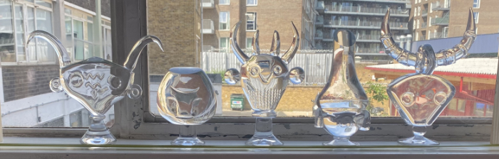 A selection of clear glass masks stood in a window showing interesting reflections through the glass.