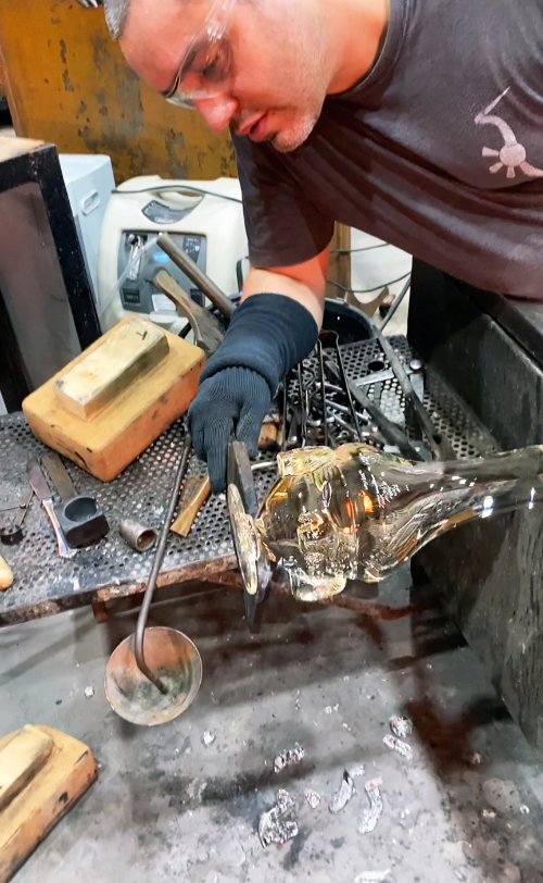 Theo Brooks shaping molten clear glass mask base using glass tools.